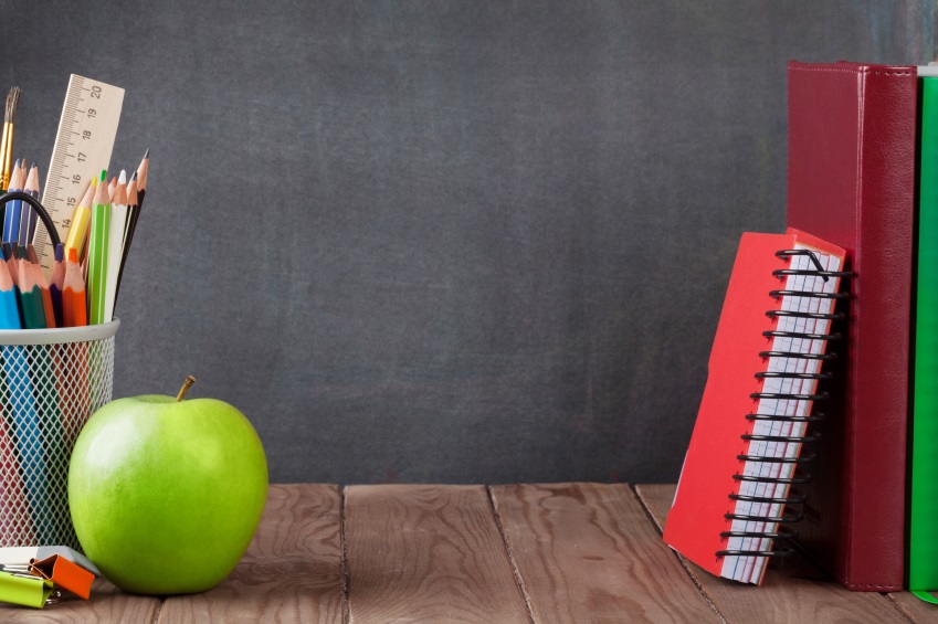 School and office supplies and apple on classroom table in front of blackboard. View with copy space