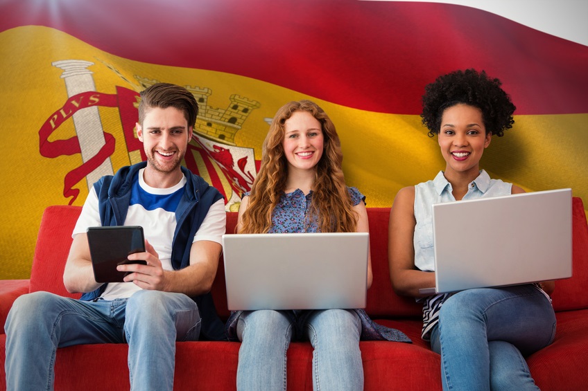 Young adults using electronic devices on couch against digitally generated spanish national flag