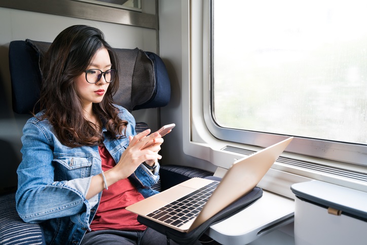 Cute Asian woman using smartphone and laptop on train